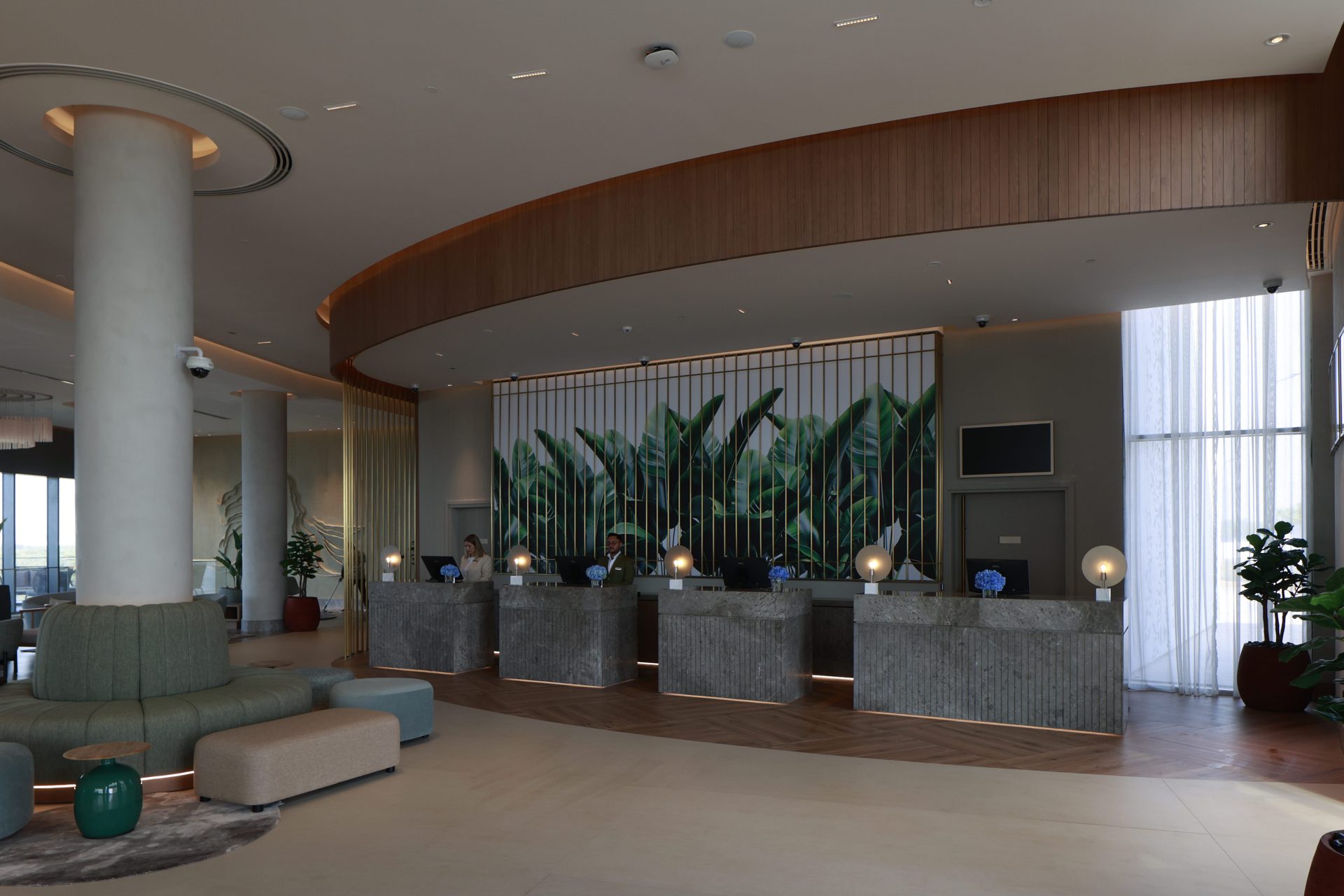 Rotana Ras Al Khaimah reception before the refresh — dim, flat lighting and colour cast across the stone check-in desks and banana-leaf artwork behind them