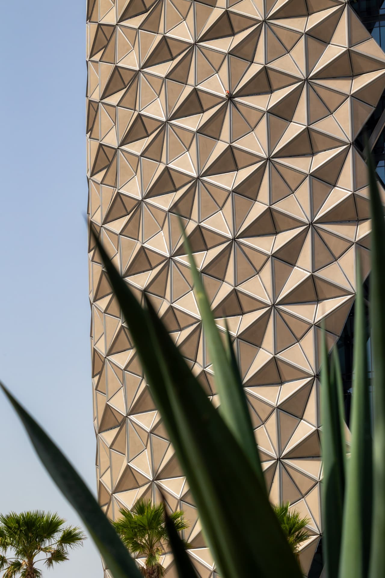 Vertical view of the ADIC tower's panels shifting from deep shadow to bright sunlight across the curve of the facade
