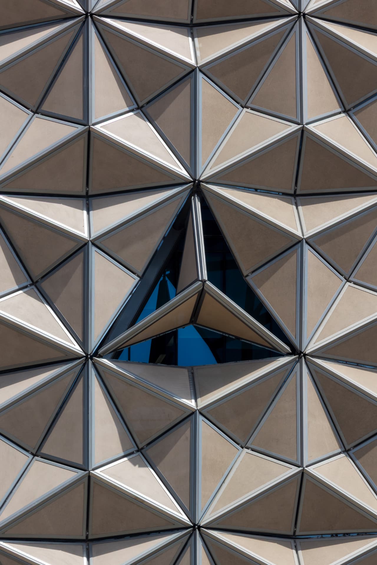 Straight-on macro crop of the ADIC Headquarters facade's repeating triangular panels in hard midday light