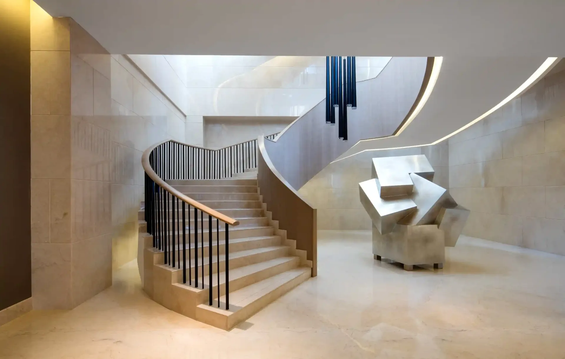 Sculptural interior staircase curving through a full-height atrium, handrail catching light from a rooflight above