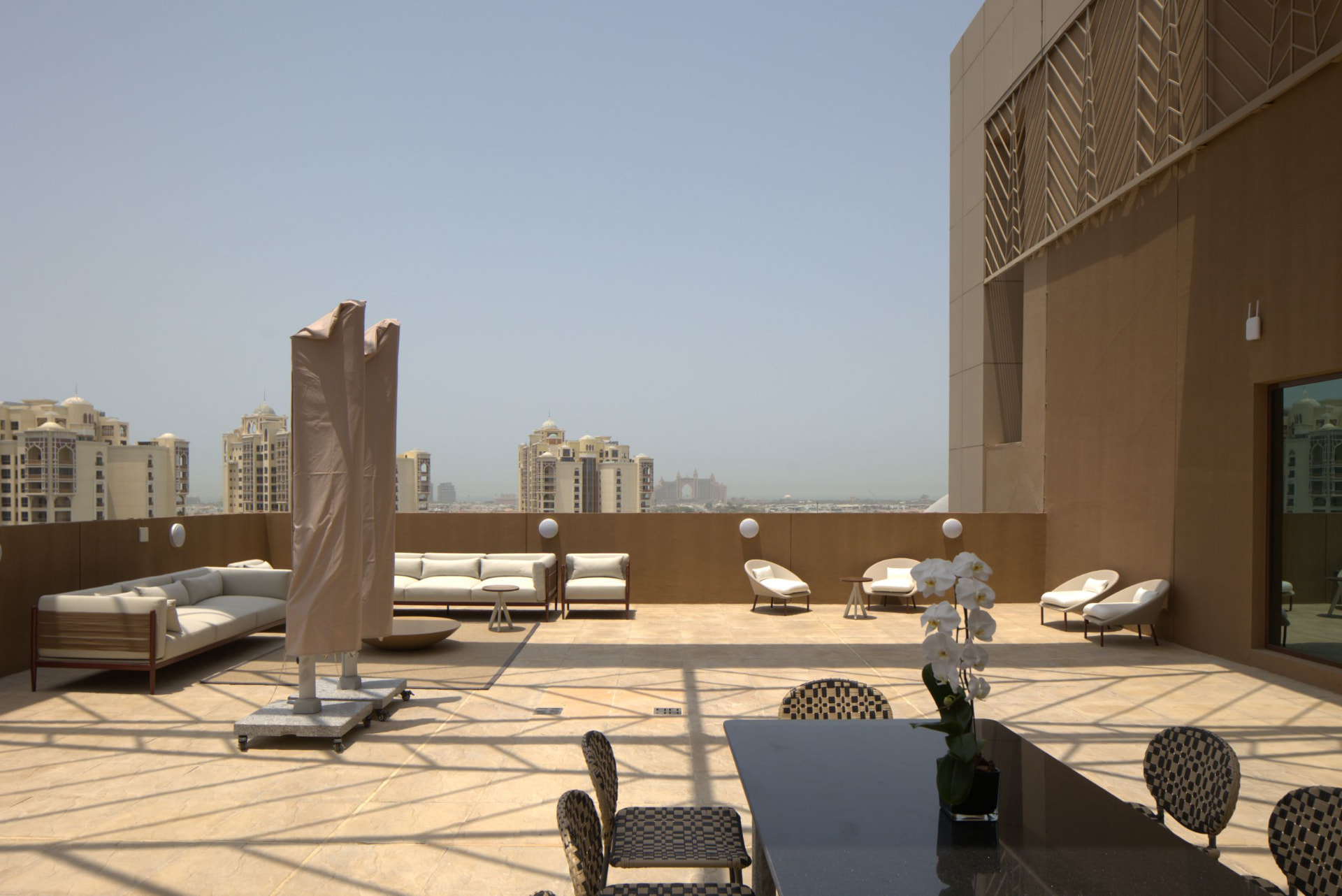 Cheval Maison The Palm terrace lounge before the photography refresh — off-axis framing with a covered parasol crossing the frame and hazy skyline