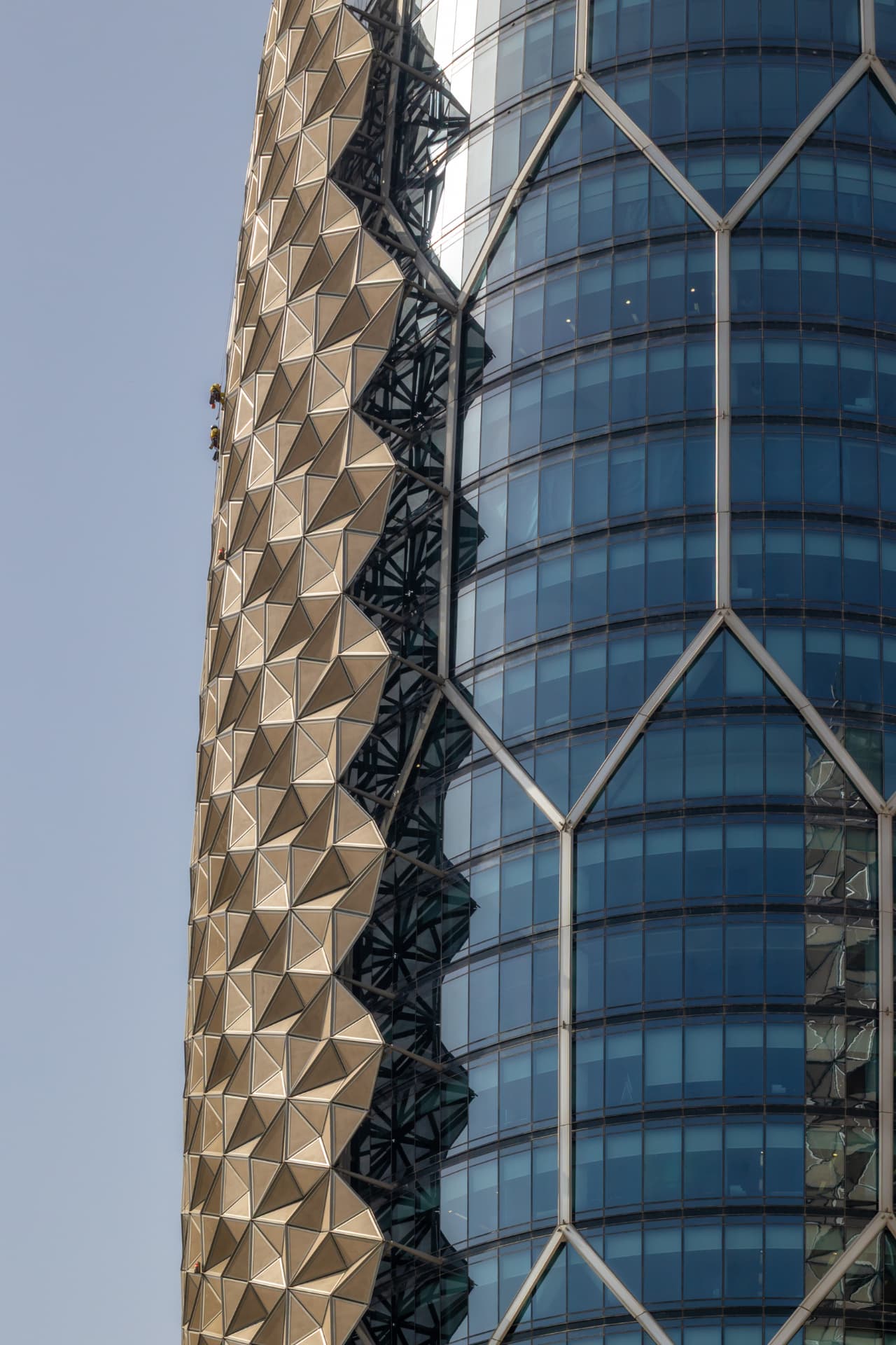 Two facade maintenance technicians in yellow safety gear on rope access descending the ADIC tower's panelled facade