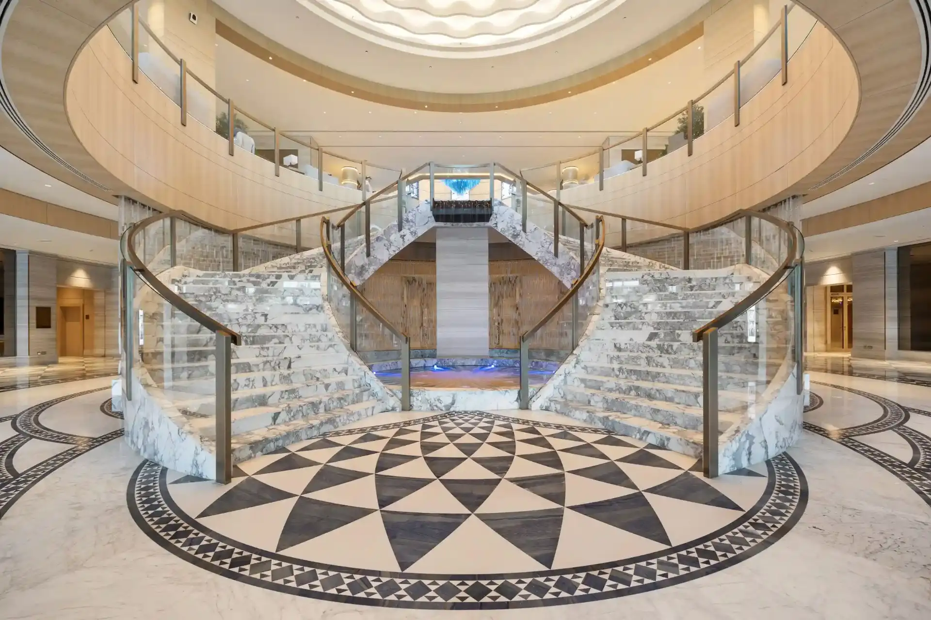 Sweeping marble staircase in a residential entrance hall, veining and brass handrail lit by soft daylight from above
