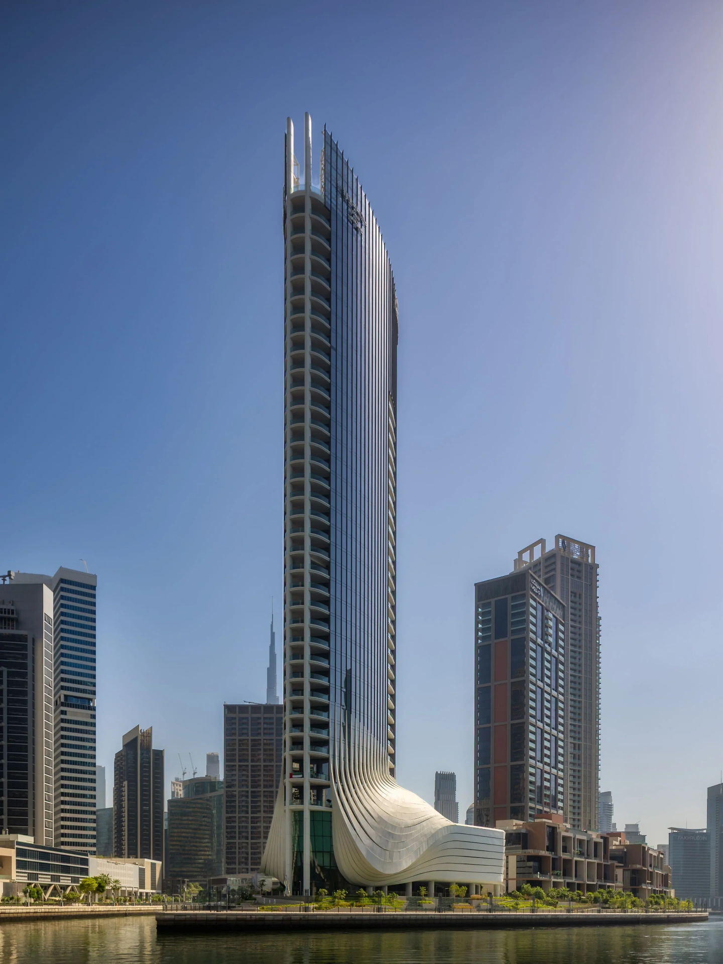 Curved residential tower shot from street level, balcony lines sweeping upward against clear afternoon sky