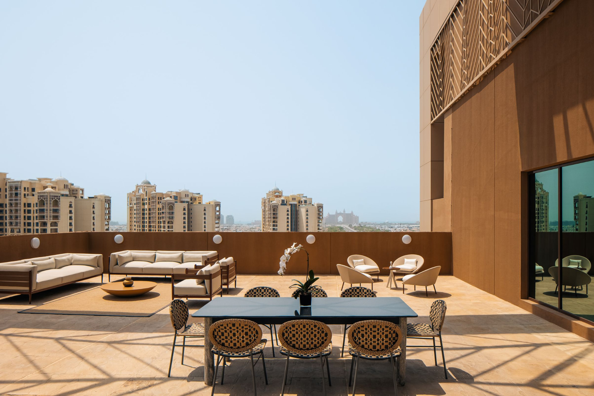 Cheval Maison The Palm terrace lounge after the photography refresh — symmetrical framing of the dining table and sofas with the Palm Jumeirah skyline and Atlantis beyond
